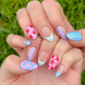 Hand-Painted press-on nails with various bright designs in red, light pink, and light blue colors. The press-on nail designs include stars, blueberries, dots, and checkers. 
