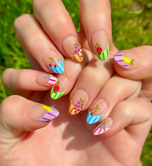 Fruity Press On Nails with vibrant colors. Nails have colorful french striped tips and different fruits on each nail including grapes, cherries, lemon, blueberries, and strawberries. Hands are stacked on top of each other to display each press on design.