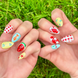 Two hands displaying summer press on nails with vibrant, fun designs. Nail designs include a lobster, stars, cherries, gingham, fish, watermelon, and blueberries. Nail colors include red, white, orange, light blue, green, and yellow. The two hands are displaying the press on nails on a grassy summer background.