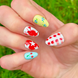 One hand displaying summer press on nails with vibrant, fun designs. Nail designs include a lobster, stars, cherries, gingham, and blueberries. Nail colors include red, white, orange, light blue, green, and yellow. The two hands are displaying the press on nails on a grassy summer background.