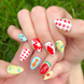 Two hands displaying summer press on nails with vibrant, fun designs. Nail designs include a lobster, stars, cherries, gingham, fish, watermelon, and blueberries. Nail colors include red, white, orange, light blue, green, and yellow. The two hands are displaying the press on nails on a grassy summer background.