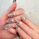 Hands with hand painted salon press-on nails in long almond shape, featuring black and silver polka dots, bows, and french tips