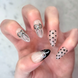 Hand with decorative nail art on salon press-ons featuring  black and silver bows, black polka dots, and black french tips with silver bow detail