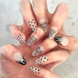 Two hands interlocked with hand painted salon press-on nails in long almond shape, featuring black and silver polka dots, bows, and french tips