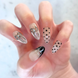 Left Hand with hand painted salon press-on nails in long almond shape, featuring black and silver polka dots, bows, and french tips