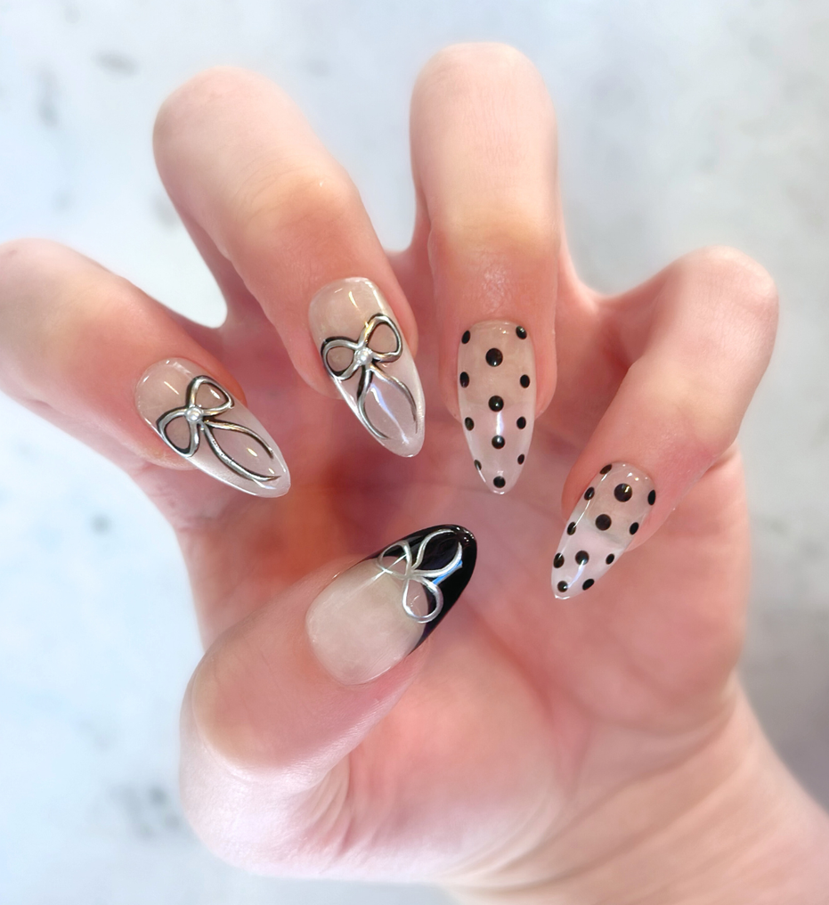 Left Hand with hand painted salon press-on nails in long almond shape, featuring black and silver polka dots, bows, and french tips