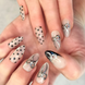 Close up of two hands with gel painted salon press-on nails in long almond shape, featuring black and silver polka dots, bows, and french tips