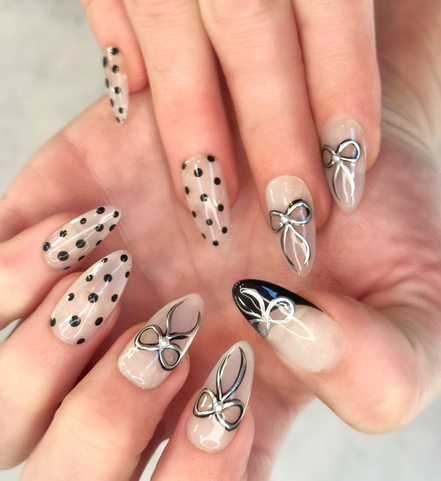 Close up of two hands with gel painted salon press-on nails in long almond shape, featuring black and silver polka dots, bows, and french tips