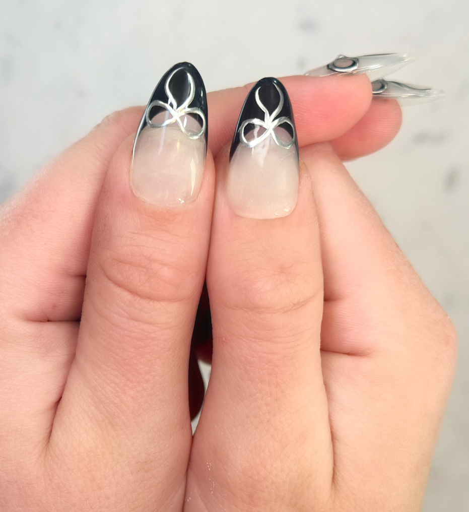 Two thumbs showing hand painted press-on nails in long almond shape, with black french tips and silver bow detailing