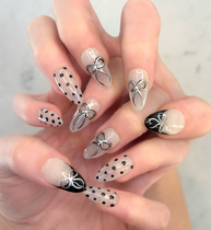 Two hands interlocked showing hand painted luxury press-on nails in long almond shape, featuring black and silver polka dots, bows, and french tips