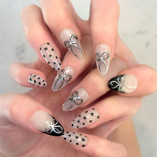 Two hands interlocked showing hand painted luxury press-on nails in long almond shape, featuring black and silver polka dots, bows, and french tips