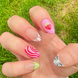 Hand-Painted acrylic press-on nails with vibrant colors and designs including strawberries, stars, gingham, zebra print, and french tips. The nail colors are red, light green, light pink, zebra print, and silver details. Two hands and nails are displayed on a grassy summer background.